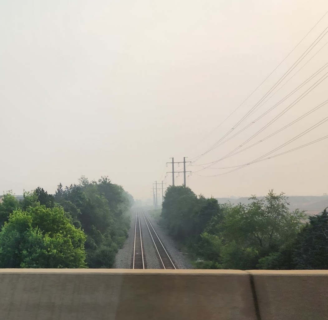 Railroad vanishing into mist under hazy sky, seen from concrete road barrier.