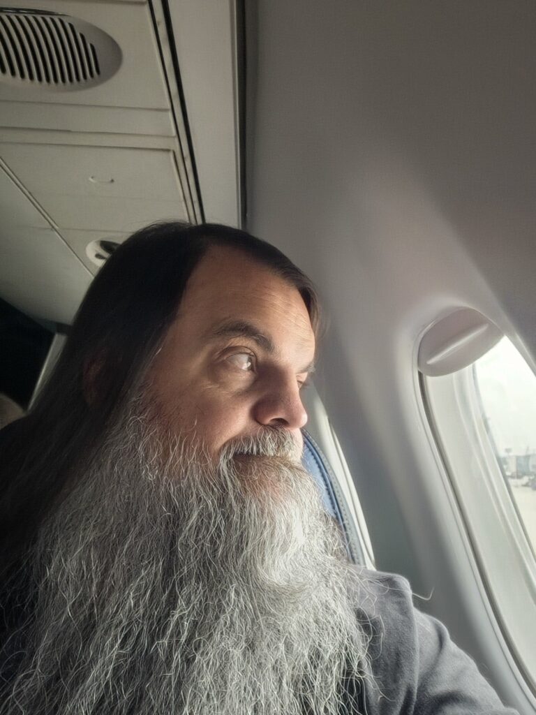 Bryan on a plane with beard looking out window
